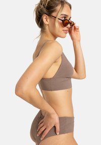 Bralette marrone strutturato con spalline sottili, abbinato a pantaloni a vita alta coordinati. Modella che indossa occhiali da sole tartarugati.