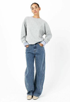 Grauer Pullover mit langen Ärmeln, blau gestreifte Bündchen; kombiniert mit übergroßen hellblauen Jeans aus Denim, mit lockerem Sitz und geradem Bein.