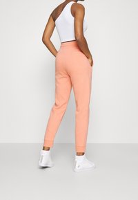 Peach jogger pants with side pockets, tapered legs, and ribbed cuffs, paired with white high-top sneakers and a fitted white tank top.