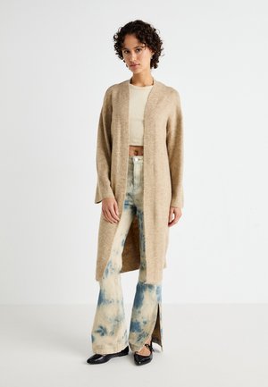 Beige knitted cardigan with open front, long sleeves, and textured fabric, paired with light denim flared pants featuring blue tie-dye patterns.