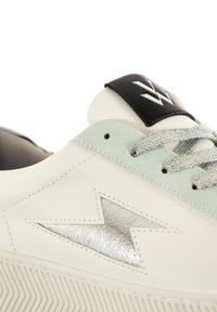 Zapatilla de cuero blanco con acentos en menta clara, detalles metálicos plateados, suela de goma texturizada y cordones reflectantes. Logo negro en la lengüeta.