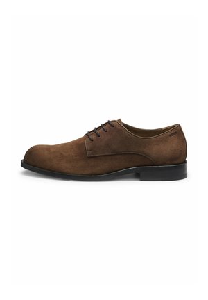 Chaussure habillée pour homme en daim marron à lacets, semelle noire, petit talon, et coutures latérales discrètes sur fond blanc.