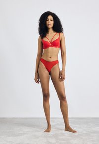 Red lace bra with dual straps, underwire support, and matching red high-cut briefs, featuring a smooth texture and minimal design.