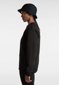 Zwarte sweatshirt met een relaxte pasvorm, lange mouwen en ribgebreide manchetten, gecombineerd met een zwarte bucket hat. Huidige textuur en minimale ontwerp kenmerken.