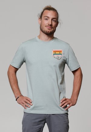 T-shirt bleu clair à manches courtes en coton, ornée d'un design de poche graphique avec une cassette rétro en orange, rose et bleu.