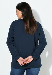 Langarm-Hemd in Marineblau aus weichem Stoff, mit lockerem Schnitt, rundem Halsausschnitt und seitlichen Schlitzen. Kombiniert mit blauen Jeans.