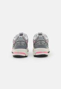 Un paio di scarpe sportive grigie e rosa viste da dietro su uno sfondo bianco.
