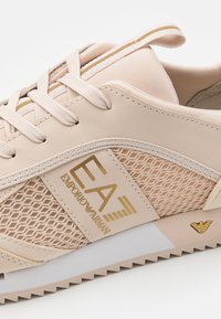 Pink and beige sneaker with a mesh panel, textured material, gold accents, and logo. Features round laces and a ridged sole.