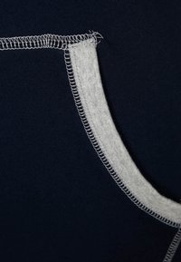 Marinblått tyg med grå sömnadsdetaljer. Har en slät textur och synliga sömmar som framhäver plaggets konstruktionsmoment.