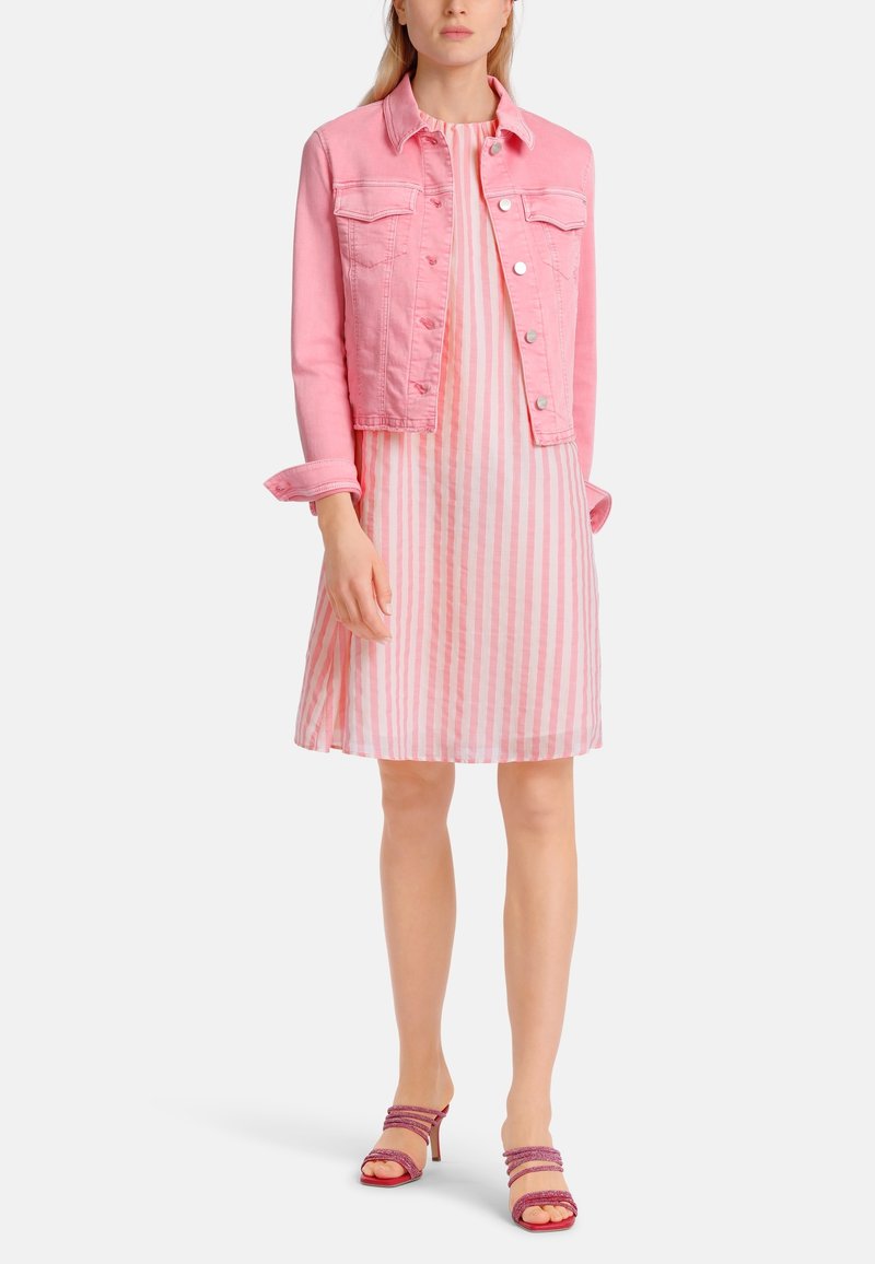 Femme portant une veste en jean rose par-dessus une robe sans manches rose et blanche à rayures jusqu’aux genoux, avec des sandales à talons hauts roses à brides.