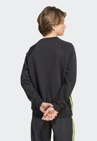Sweatshirt preto com decote redondo, mangas raglan e riscas laterais em verde néon. O material parece suave com uma textura lisa.