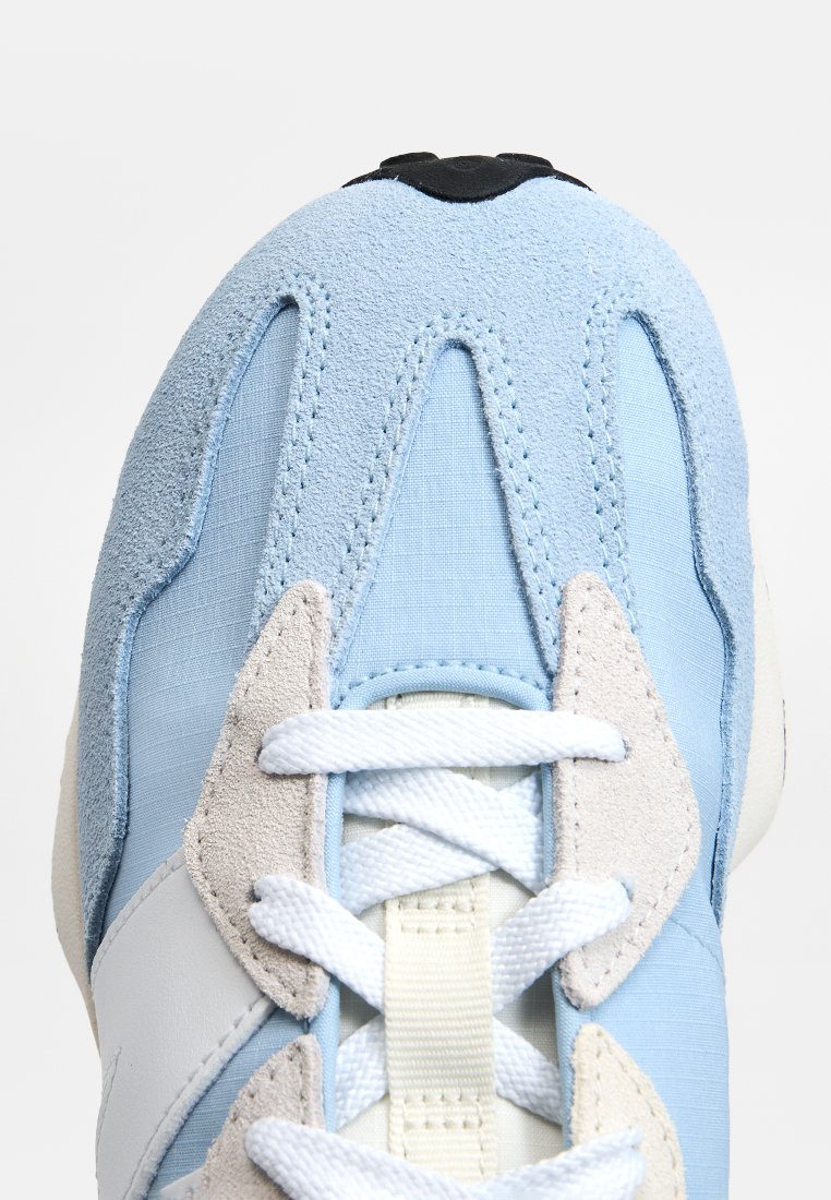 Zapatillas de deporte azul claro que presentan una mezcla de tela suave y ante, con un diseño texturizado, cordones blancos y una suela de goma negra.
