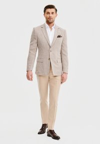 Beżowa marynarka w kratę z dwoma guzikami, biała koszula, jasnobeżowe spodnie, ciemnobrązowe eleganckie buty, z poszetką.