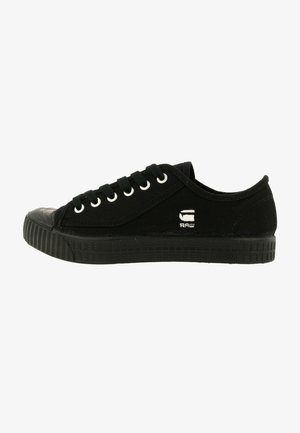 Czarny niski tenis z materiału z czarną gumową podeszwą, czarnymi sznurowadłami, metalowymi przelotkami i małym białym logo "RAW" z boku.