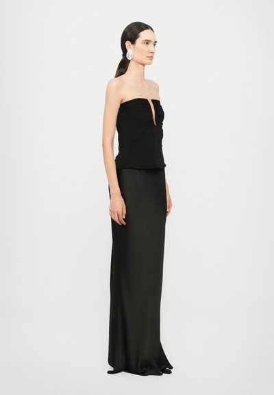 Vestido negro sin tirantes con un corsé ajustado que presenta detalles recogidos y un corte en forma de llave. La falda cae hasta el suelo con una textura suave.