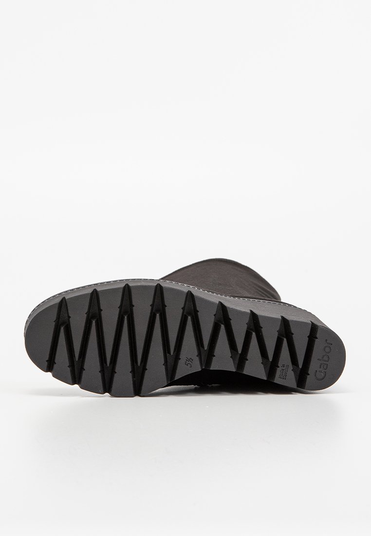 Schwarze Knöchelstiefel mit einer strukturierten Gummisohle, die ein Zickzackmuster für besseren Halt aufweist. Das Obermaterial besteht aus glattem Material ohne sichtbare Akzente.
