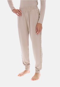 Beżowe, miękkie spodnie dresowe z elastycznym paskiem w talii i bocznymi kieszeniami. Ozdobione falistymi akcentami wzdłuż zewnętrznych szwów.