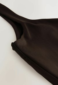 Tejido negro y elástico con una textura suave. Cuenta con una correa ancha y un escote redondeado. Detalles de costura a lo largo de los bordes.