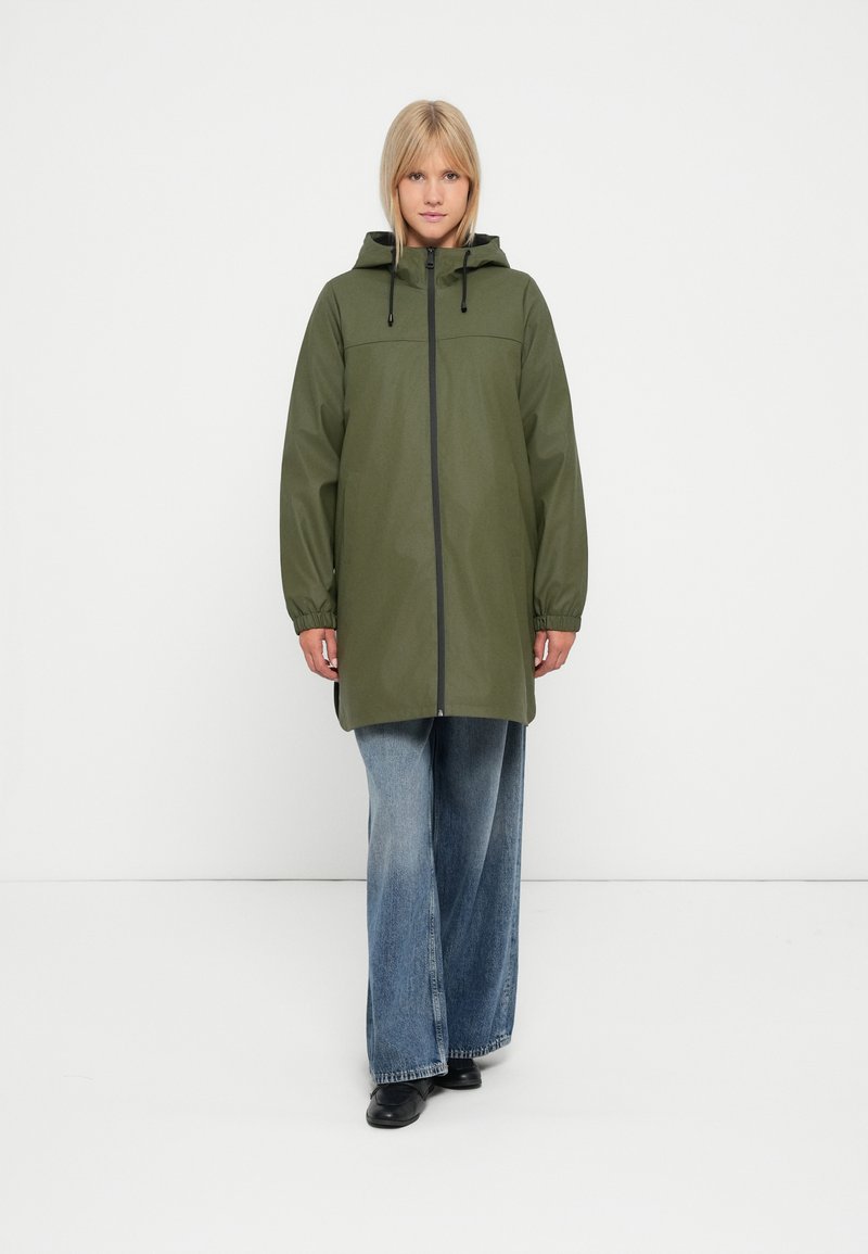 Grønn, hettejakke med vanntett materiale, glidelås, elastiske mansjetter og frontlommer, sammen med brede, blå denimjeans.