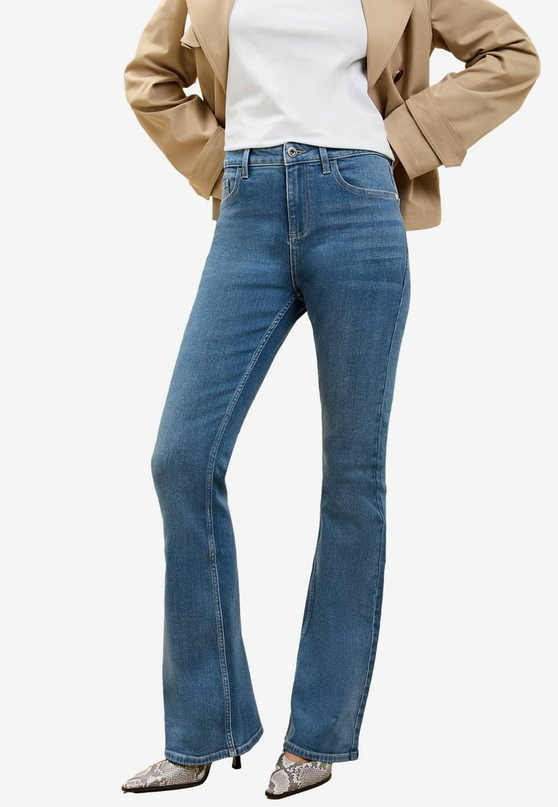 Modre flare kavbojke iz denima z visokim pasom, z zapiranjem na sprednjem gumbu in stranskimi žepi. Kombinirane z čevlji z peto v kačjem vzorcu.