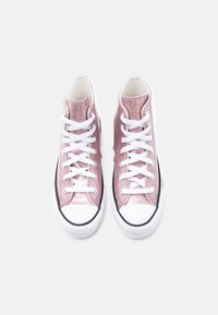 Ζευγάρι από λαμπερά ροζ ψηλοτάκουνα αθλητικά παπούτσια με λευκά κορδόνια και λαστιχένιες άκρες δαχτύλων, σε λευκό φόντο, σε θέα από ψηλά.