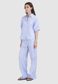 Hellblau gestreiftes Hemd mit kurz gerollten Ärmeln, kombiniert mit passenden weit geschnittenen Hosen. Der Stoff wirkt glatt und weich.