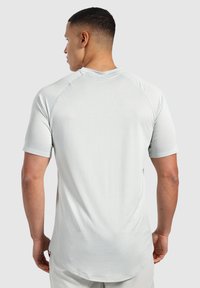 Jasnoszara koszulka sportowa z krótkimi rękawami, wykonana z teksturowanej tkaniny i z zaokrąglonym dołem. Zawiera rękawy raglanowe, co zapewnia swobodę ruchów.