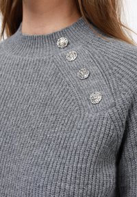 Gray knitted sweater featuring a round neck and four decorative rhinestone buttons along the shoulder. Soft texture with ribbed detailing.