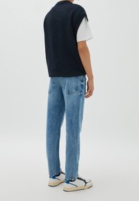 Marinblå stickad väst över vit t-shirt, kombinerad med ljusblå denimjeans och vita sneakers med blå detaljer och strukturerade sulor.