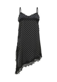Robe nuisette noire en soie à pois blancs, fines bretelles, bordure en dentelle au niveau du décolleté et ourlet asymétrique sur fond blanc.
