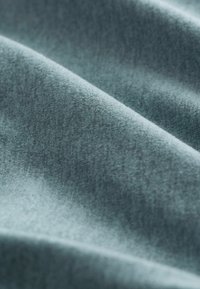 Zachte, gestructureerde stof met een matte afwerking in een gedempte teal-kleur, met zachte plooien en een gladde oppervlakte.