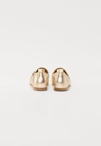 Ballerines métalliques dorées avec une finition lisse, un bout arrondi et un design minimal, présentant un petit talon et sans quincaillerie visible.