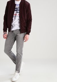 Mörk burgundy bomberjacka med en slät textur, grå grafisk t-shirt, ljusgrå slim fit jeans och vita sneakers.