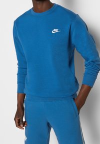 Sweatshirt bleu en tissu doux, avec un col ras du cou, des poignets côtelés et un logo Nike blanc sur la poitrine. Stylé avec un pantalon assorti.