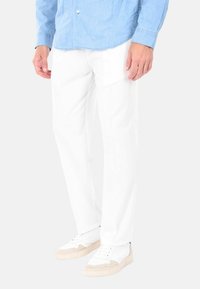 Pantaloni in cotone bianchi con design a gamba dritta, abbinati a una camicia azzurra chiara con bottoni e sneakers bianche. Nessun motivo visibile.