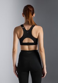 Svart sportsbh med racerback-design, med et sirkulært utsnitt bak; kombinert med høyt midjebelte svarte leggings.