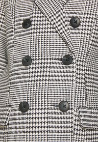 Doppelreihiger Blazer in Schwarz-Weiß mit Hahnentrittmuster, aus glattem Stoff, mit strukturierten Revers und schwarzen Knöpfen.