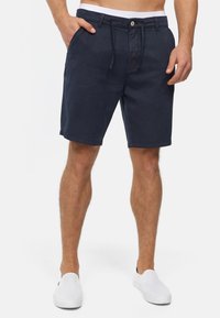 Marineblå shorts lavet af stof, med forlommer, knaplukning og elastisk talje med snor. Glat tekstur uden mønstre.