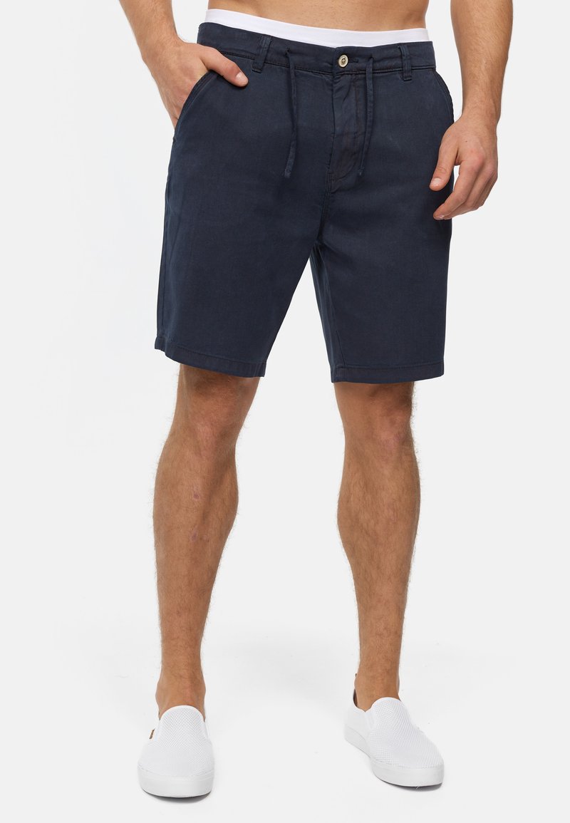 Marineblå shorts lavet af stof, med forlommer, knaplukning og elastisk talje med snor. Glat tekstur uden mønstre.