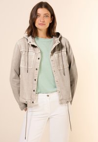 Light gray denim jacket with a hood, buttoned front, and two chest pockets. Worn over a mint green shirt and white pants. Smooth texture.