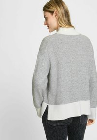Grijze gebreide trui met een witte geribbelde kraag en zoom, featuring een cropped achterkant en zijsplitten voor comfort. Gelaagd materiaal met een zachte afwerking.