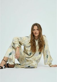 Ľahká loungewear sada v tie-dye dizajne v jemnej béžovej farbe s zelenými a hnedými akcentmi; voľný strih, dlhé rukávy a široké nohavice s elastickými manžetami.