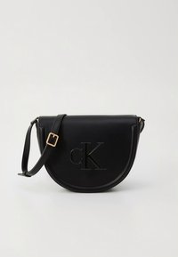 Czarna skórzana torba na ramię o zakrzywionym kształcie, z tłoczonym logo „cK”, złotymi elementami i regulowanym paskiem.
