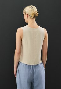Top beige sin mangas con cuello redondo y dobladillo recto, hecho de un tejido texturizado, combinado con pantalones sueltos azul claro.