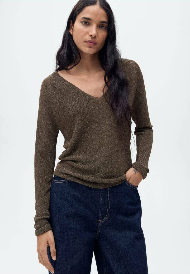 Brązowy sweter z długim rękawem i dekoltem w serek, wykonany z fakturowanego dzianego materiału. W połączeniu z ciemnymi dżinsami o luźnym kroju.