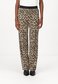Leopard print sweatpants with a black elastic waistband, featuring a loose fit and soft texture, worn with black footwear.