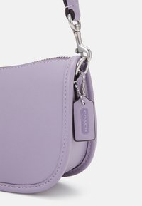 Purple leather bag with a smooth texture, curved shape, and silver hardware. Features a small tag with "COACH" logo attached.