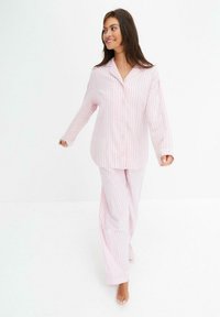 Set di pigiama a righe rosa e bianche con camicia abbottonata e pantaloni larghi; il tessuto sembra morbido con una superficie liscia.