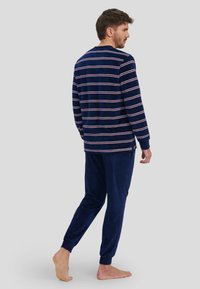 Conjunto de ropa de casa a rayas en navy, hecho de una tela suave. Camiseta de manga larga con rayas blancas y rojas; pantalones elásticos a juego con puños y bolsillos laterales.