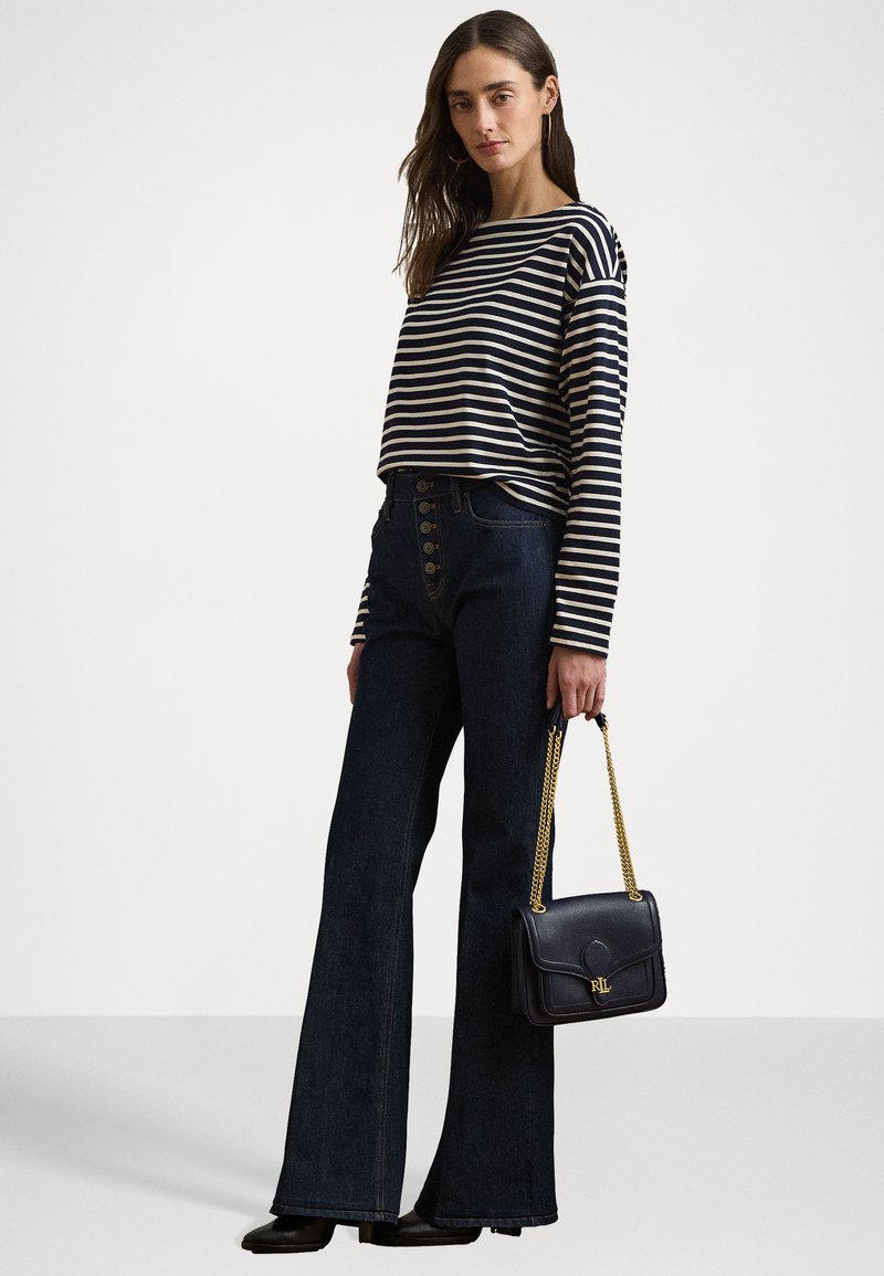 Top a maniche lunghe a righe in blu navy e crema, pantaloni flare in denim scuro a vita alta con dettaglio dei bottoni, e una borsa nera con catena dorata.